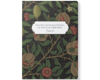 May include: A rectangular notebook with a black background featuring a botanical pattern of green leaves, brown pomegranates, and red flowers. A white label in the centre displays the text: I love the Lord, because He hears my voice & my supplications. Psalm 116:1.
