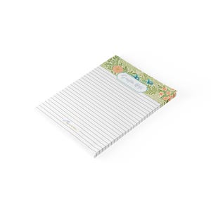 May include: A rectangular notepad with lined white paper. The top header features a green botanical pattern with orange flowers and blue accents. A central label reads Scripture Notes, and a small logo is printed in the bottom left corner.