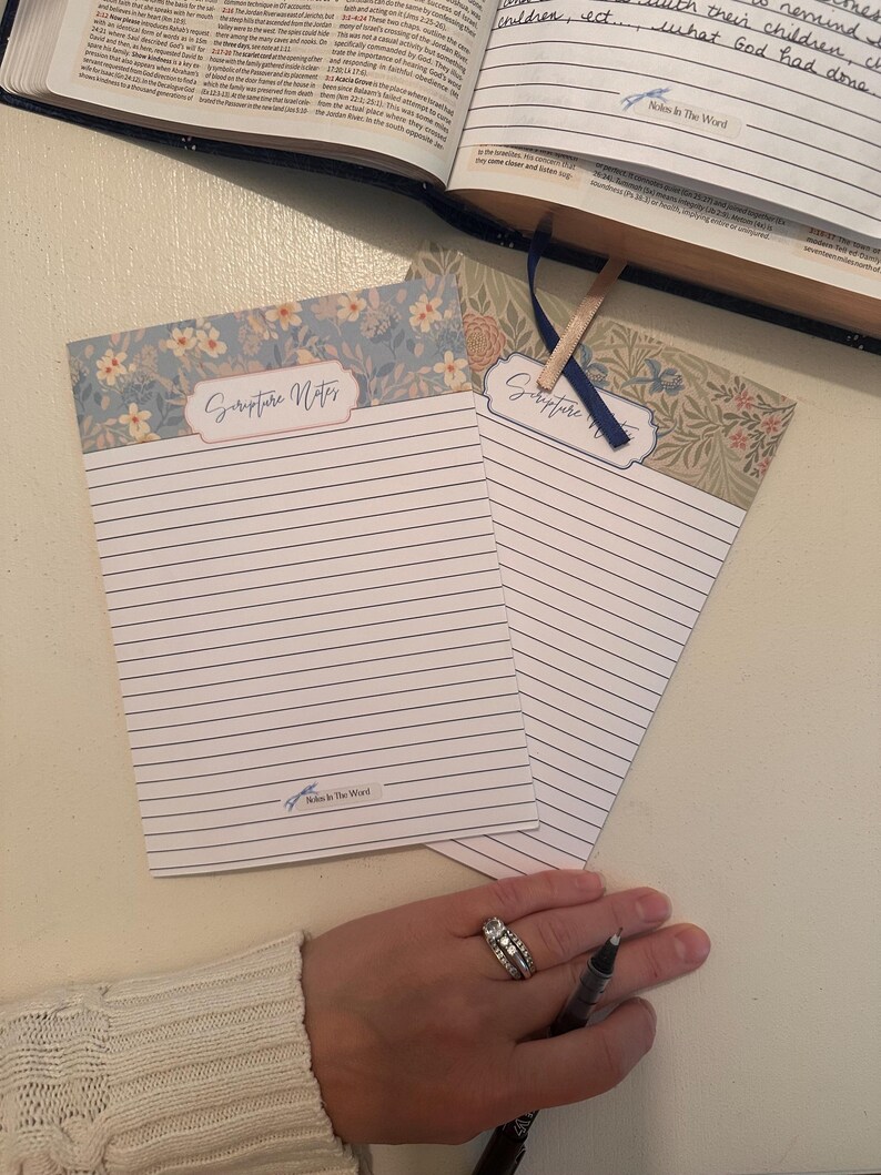 Pu&ograve; includere: Due blocchi per appunti rettangolari in carta con linee orizzontali e motivi floreali nella parte superiore. Ogni blocco presenta un'etichetta con il testo Scripture Notes e un piccolo logo in basso con il testo Notes In The Word.