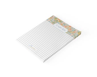 May include: A rectangular notepad with horizontal black lines for writing. The top section features a floral pattern in shades of orange, blue, and green. The text Scripture Notes is printed in a white label shape, and Faith in the Word is at the bottom.