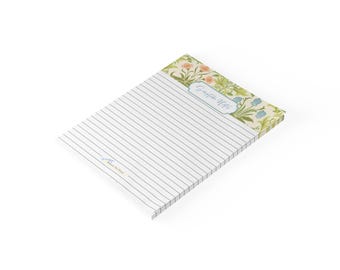 May include: A rectangular notepad with horizontal black lines on a white background. The top section features a floral pattern in shades of green, orange, and blue, with a central label containing the text Scripture Notes in blue cursive script.