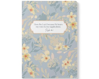May include: A rectangular notebook with a light blue background featuring a pattern of pale yellow flowers and muted green leaves. A central white label with a thin orange border displays the text: I love the Lord, because He hears my voice & my supplications. Psalm 116:1.