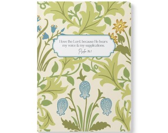 May include: A rectangular notebook with a cream background featuring a repeating pattern of green leaves, yellow flowers, and blue bell-shaped blossoms. A central white label contains the text: I love the Lord, because He hears my voice & my supplications. Psalm 116:1.