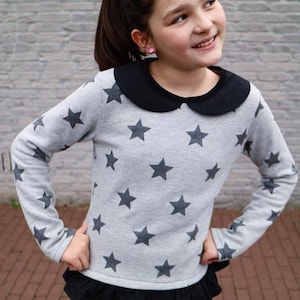 May include: A gray long-sleeved shirt with black star print and a black peter pan collar. The shirt has a black ruffle trim at the bottom and is worn with blue jeans.
