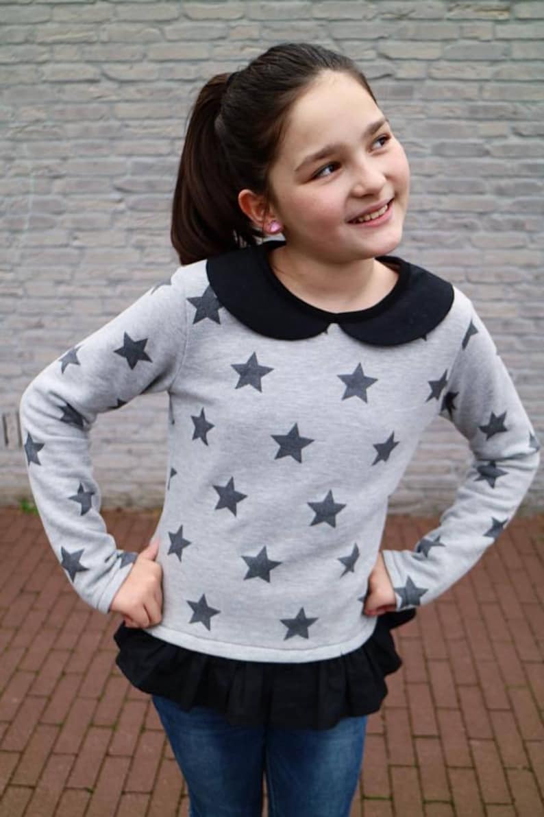 May include: A gray long-sleeved shirt with black star print and a black peter pan collar. The shirt has a black ruffle trim at the bottom and is worn with blue jeans.