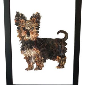 May include: Framed artwork of a Yorkshire Terrier dog made from various brown and tan buttons. The dog is depicted in a standing pose, with a fluffy coat and a curled tail. The artwork is set against a white background within a black frame.