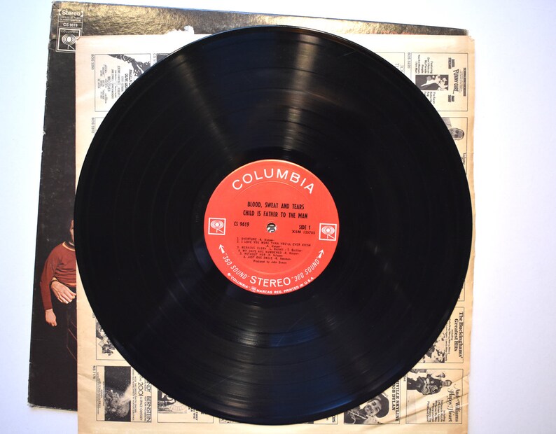 May include: A black vinyl record with a red label that says "Columbia" and "Blood, Sweat and Tears Child is Father to the Man". The record is on a white background.