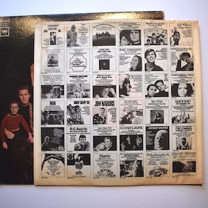 May include: A black and white vinyl record album cover featuring two men in a black and brown patterned shirt and a brown shirt. The back of the album cover features a grid of album covers with various artists and album titles.
