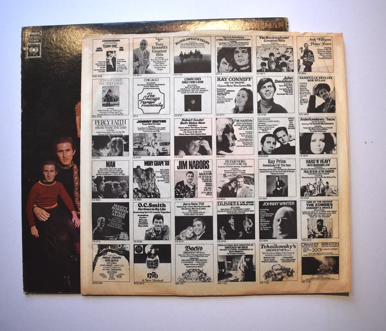 May include: A black and white vinyl record album cover featuring two men in a black and brown patterned shirt and a brown shirt. The back of the album cover features a grid of album covers with various artists and album titles.