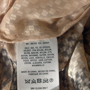 Może przedstawiać: Zbliżenie metki z tkaniny z tekstem. Etykieta zawiera skład tkaniny: 73% nylon, 27% rayon i 100% bawełniana koronka. Zawiera r&oacute;wnież instrukcje pielęgnacji i pochodzenie odzieży.