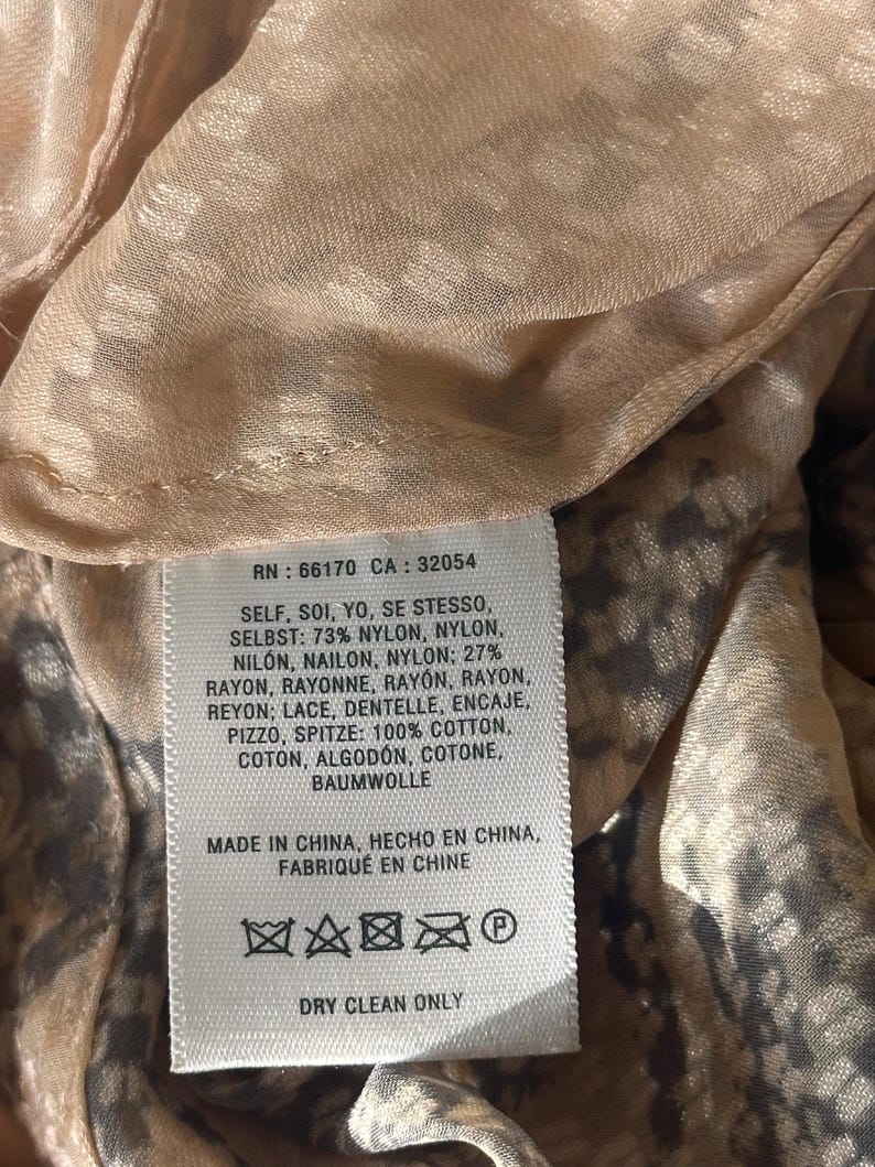 Może przedstawiać: Zbliżenie metki z tkaniny z tekstem. Etykieta zawiera skład tkaniny: 73% nylon, 27% rayon i 100% bawełniana koronka. Zawiera r&oacute;wnież instrukcje pielęgnacji i pochodzenie odzieży.
