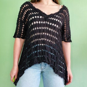 Op de afbeelding: Een zwart gehaakt top met een losse pasvorm en een V-hals. De top heeft een distressed look met een rafelige zoom.