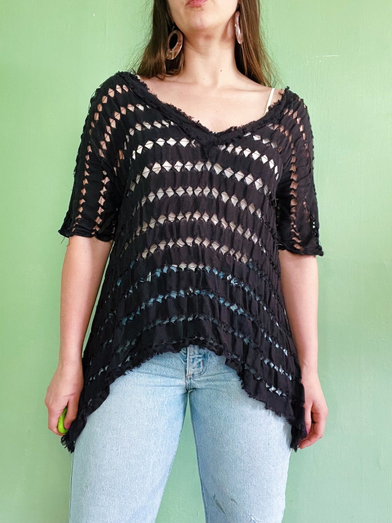 Op de afbeelding: Een zwart gehaakt top met een losse pasvorm en een V-hals. De top heeft een distressed look met een rafelige zoom.
