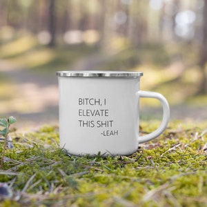 May include: White enamel mug with a silver rim and handle. The mug features the text "BITCH, I ELEVATE THIS SHIT -LEAH" in black. The mug is sitting on a bed of green moss.