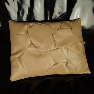 May include: A tan-colored pillow with a geometric pattern. The pillow is made of a soft, textured fabric and has a rectangular shape.