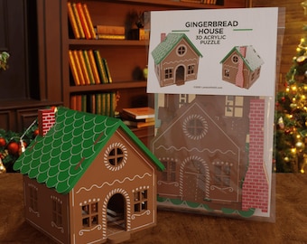 Può includere: Una casa di pan di zenzero marrone con tetto verde e finiture bianche è accanto a una confezione con un puzzle 3D in acrilico. La confezione mostra una casa di pan di zenzero con il testo "GINGERBREAD HOUSE 3D ACRYLIC PUZZLE". La casa ha un camino di mattoni rossi.