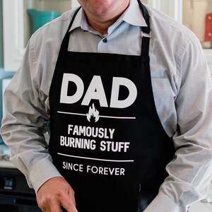 Dad. Famously Burning Stuff Since: Forever Apron / Funny BBQ Grilling Gift for Dad & Grandpa / Large 1 Size Fits All with Adjustable Neck