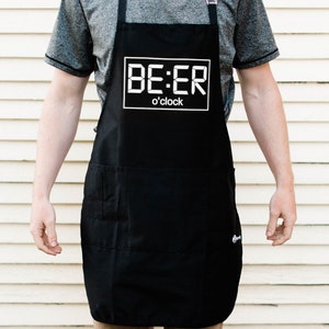 May include: A black apron with a white digital clock design that reads "BE:ER o'clock".