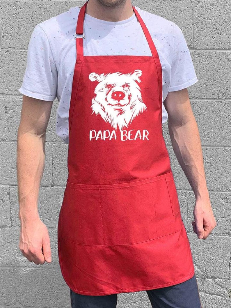 May include: Red apron with a white bear face and the text "Papa Bear" printed on the front. The apron has a large pocket on the front.
