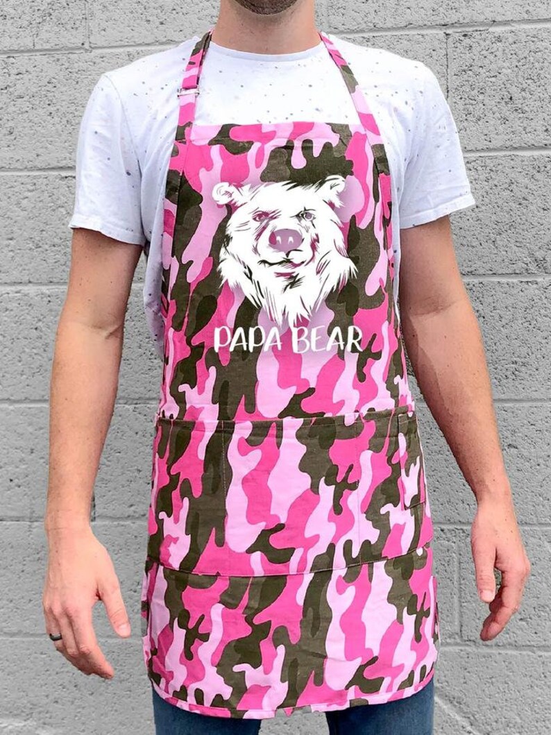 May include: Pink and green camouflage apron with a white bear graphic and the text "Papa Bear".