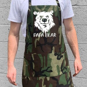 May include: A green and brown camouflage apron with a white bear graphic and the text "Papa Bear".