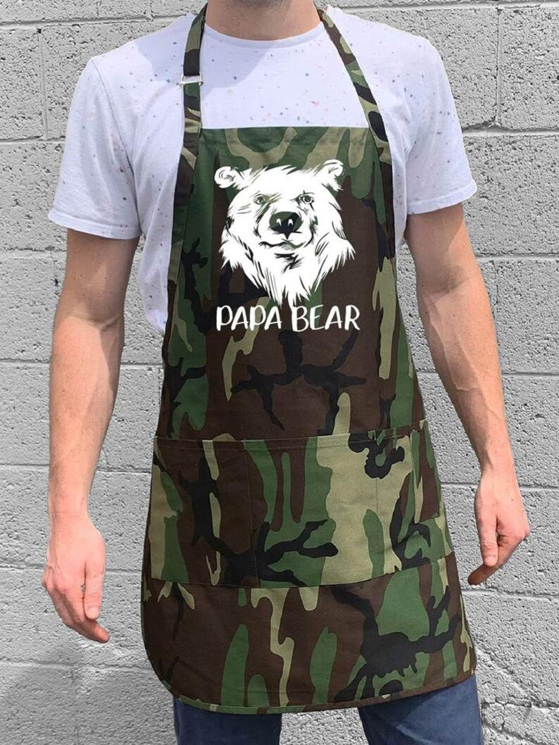 May include: A green and brown camouflage apron with a white bear graphic and the text "Papa Bear".