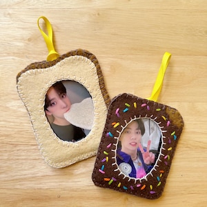 May include: Two felt photo frames shaped like toast and a chocolate-covered donut. The frames have a white oval opening for a photo. The toast frame is beige with a brown border. The donut frame is brown with colorful sprinkles around the edge.
