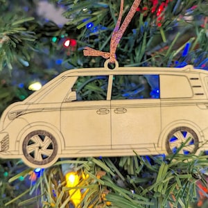 May include: A wooden Christmas tree decoration shaped like a minivan. The ornament is painted white and has black lines outlining the windows and wheels. The ornament has a brown ribbon attached to the top.