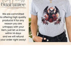 May include: A light gray t-shirt featuring a black cat with bat wings, yellow eyes, and surrounded by red and black roses. The cat is centered on the shirt, with a circular design behind it. The shirt has rolled-up sleeves.