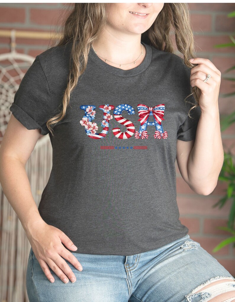 May include: A dark gray t-shirt with a graphic of the word "USA" in red, white, and blue. The letters are decorated with flowers and bows.