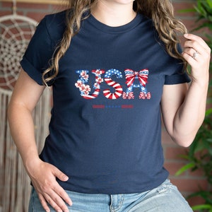 May include: A navy blue t-shirt with a graphic of the word "USA" made of red, white, and blue stars, stripes, and bows.