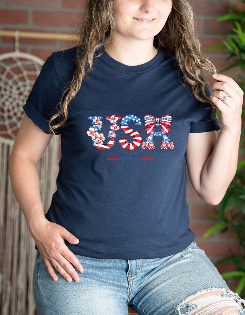 May include: A navy blue t-shirt with a graphic of the word "USA" made of red, white, and blue stars, stripes, and bows.