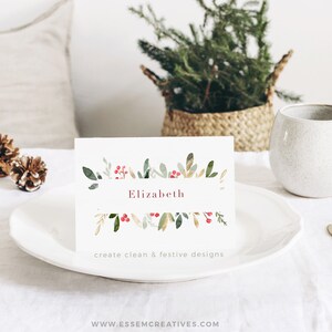 May include: A white place card with a watercolor design of green leaves and red berries. The name "Elizabeth" is written in pink lettering. The text "create clean & festive designs" is printed below the name.