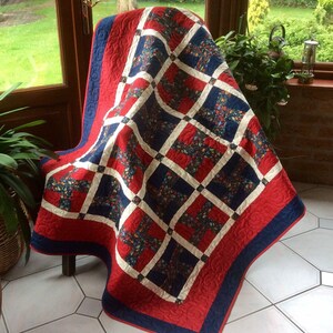 May include: A red, white and blue quilt with a floral pattern. The quilt is folded and draped over a chair.