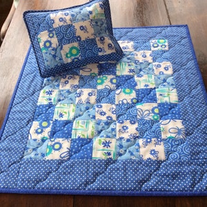 May include: A blue and white patchwork quilt with a white background and blue floral patterns. The quilt has a blue border with white polka dots. A smaller blue and white patchwork cushion is on top of the quilt.