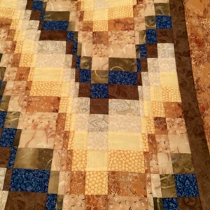 May include: A quilt made of patchwork squares in shades of brown, yellow, and blue. The squares are arranged in a diagonal pattern, creating a visually interesting design.