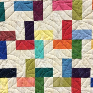 May include: A quilt made of colourful squares in various shades of red, blue, green, yellow, and purple. The squares are arranged in a pattern and sewn together with a white background.