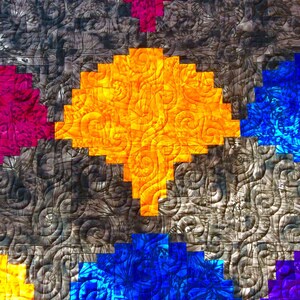 May include: A colourful quilt with a geometric pattern. The quilt is made up of squares of different colours, including purple, blue, yellow, orange, and green. The squares are arranged in a diagonal pattern, creating a sense of movement. The quilt is quilted with a swirling pattern, adding texture and depth to the design.