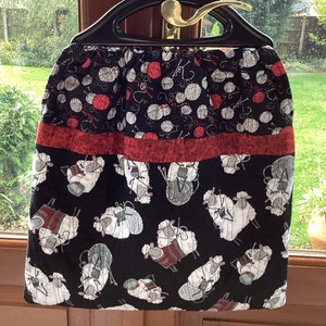 May include: Black and red fabric tote bag with a pattern of white sheep and balls of yarn. The bag has a red and white striped handle.