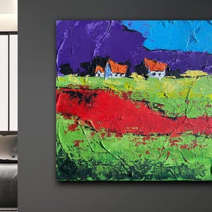 Könnte beinhalten: Quadratisches abstraktes Gemälde mit strukturierter Oberfläche. Das Kunstwerk zeigt eine Landschaft mit einer lebendigen Farbpalette. Der Himmel geht von Lila zu Blau über, mit grünen und roten Feldern. Kleine weiße Häuser mit orangefarbenen Dächern sind zu sehen.