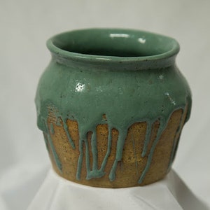 May include: A ceramic pot with a green glaze that drips down the sides. The pot is brown with a rough texture.