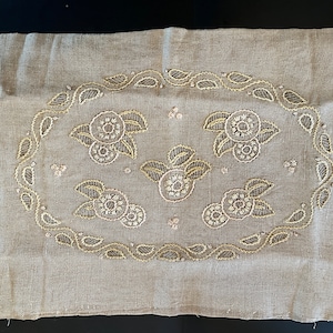 May include: A beige linen pillow cover with a gold embroidered design of flowers and leaves.