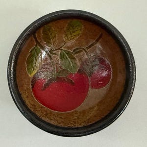 May include: A small brown ceramic bowl with a black rim, featuring a hand-painted design of red cherries with green leaves.