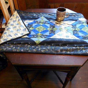 May include: A blue and white patchwork quilt table runner with a brown wooden table and a brown ceramic mug.
