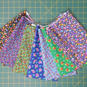May include: A collection of eight fabric swatches with floral patterns in shades of blue, green, and pink. The fabric is arranged in a fan shape on a green cutting mat.