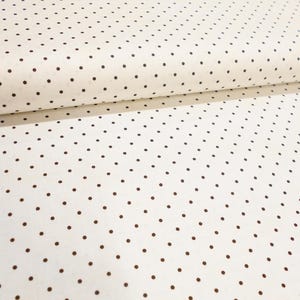 May include: Cream-colored fabric with a repeating pattern of small, evenly spaced dark brown polka dots. The fabric is folded over, showing the texture and pattern. This material is suitable for various sewing and crafting projects.