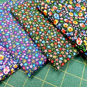 May include: Five folded fabric pieces with a floral pattern. The fabrics feature a dense arrangement of small flowers in various colors, including yellow, red, blue, and white, set against backgrounds of navy, black, and other dark hues. The fabrics are likely cotton or a similar material.