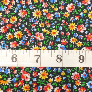 May include: Black fabric with a small floral print in shades of red, yellow, blue, and white. A measuring tape is placed on top of the fabric with the numbers 5 through 10 visible.