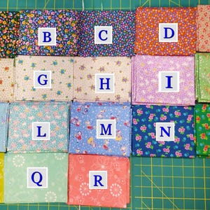 May include: A collection of fabric squares in various floral patterns and colors, including blue, pink, green, and yellow. The squares are arranged on a green cutting mat, showcasing a variety of designs.