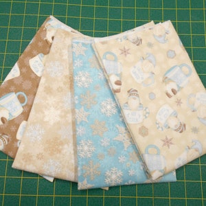 May include: Four fabric squares with winter-themed patterns. The patterns include snowflakes, snowmen, and mugs with the text "Hot Cocoa". The fabrics are in shades of brown, blue, and white.
